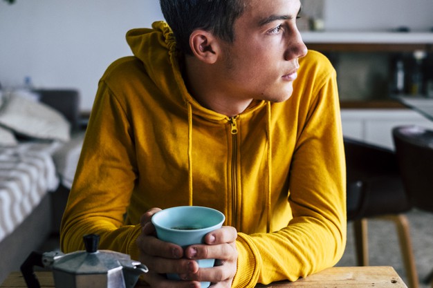  bored serious teenager male having breakfast at home alone looking outside