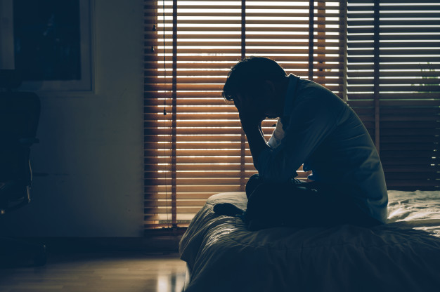 Sad businessman sitting head in hands on the bed in the dark bedroom