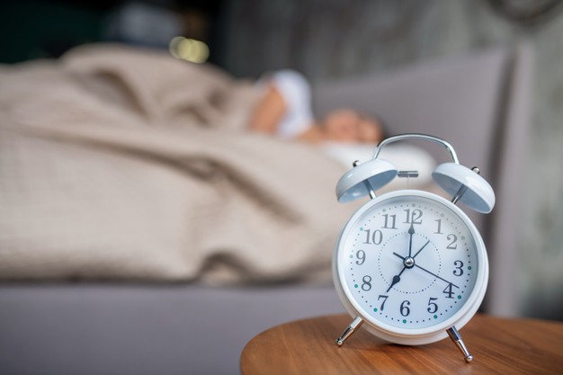 Waking up. a white mechanic alarm cloch standing near the bed 