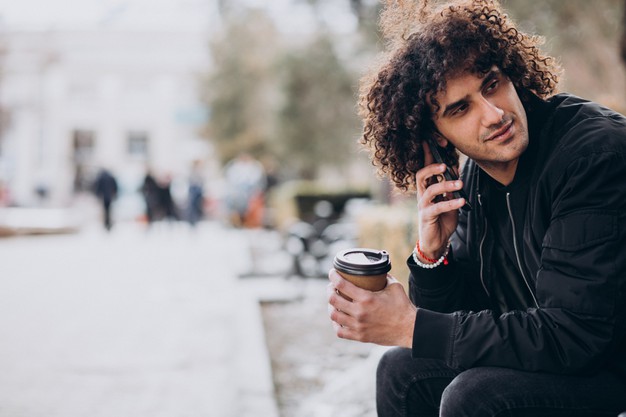young-man-with-curly-hair-drinking-coffee-talking-phone