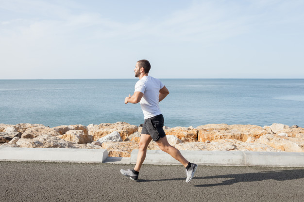 Young strong sporty man running on road along sea