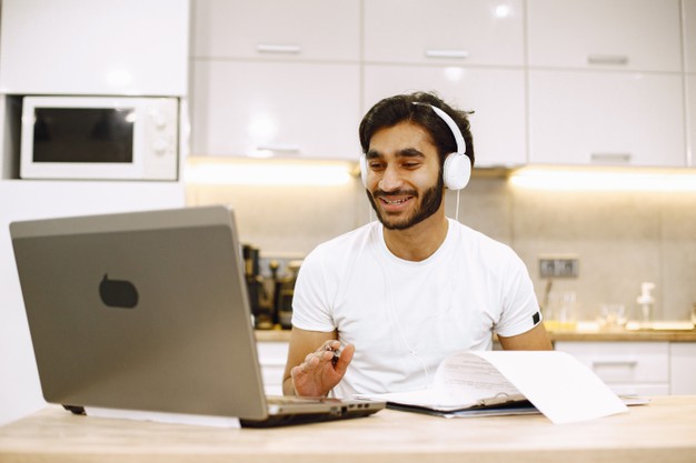 man watching online webinar, sitting in a kitchen with computer, enjoying distance learning