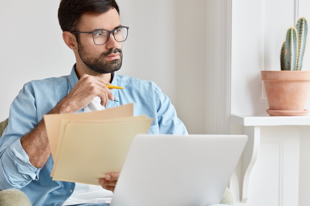 pensive man works from home, counts financial data, holds paper documents