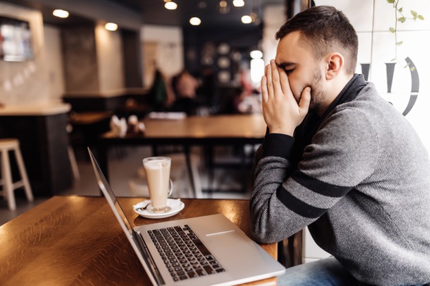 man working at laptop with head ache in cafe shop at terrace