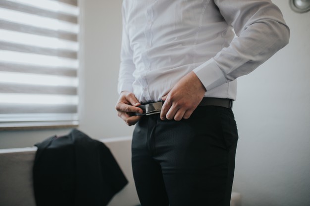 Male is fastening black belt on his trousers