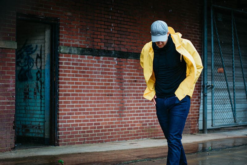 model-wearing-rains-yellow-waterproof-jacket-and-everlane-hat-