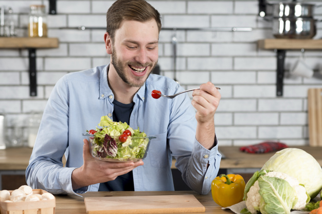 a happy man eating fresh salad in the kitchen