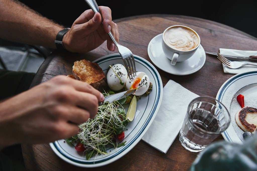 man eating salad with sprouts and eggs at restaurant