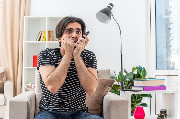 young-man-casual-clothes-holding-tv-remote-looking-stressed-scared-biting-nails-sitting-chair-light-living-room