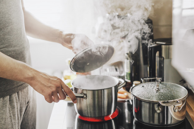 man cooking fresh food at home and opening lid of steaming pot