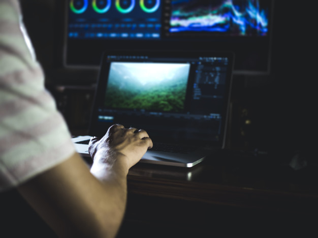 young man edit video in dark studio using color grading tools and modern equipment