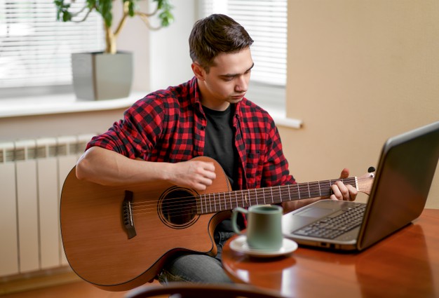 young man learns to play the guitar using the internet, laptop, online lesson 