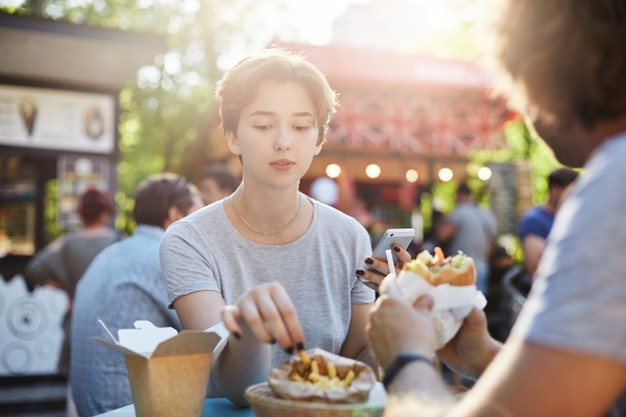 Couple eating fries and burger on a sunny summer day in park on a faire having a great time