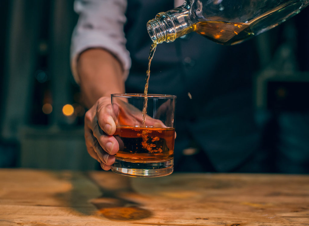Barman pouring fresh strong whiskey into a glass 