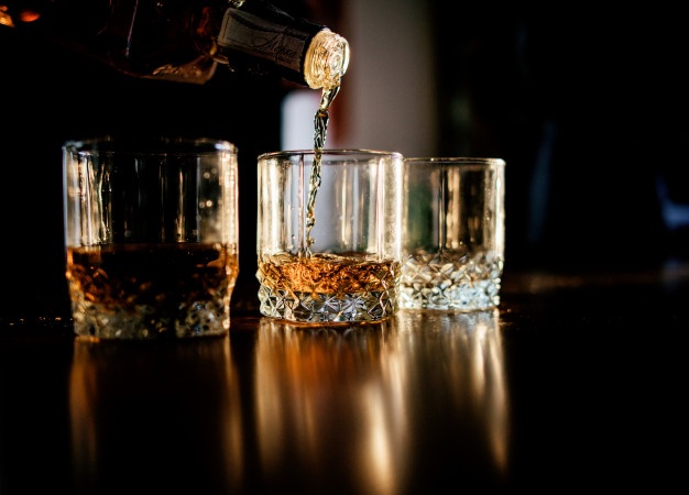 Man pours whisky in the glasses standing before a wooden table
