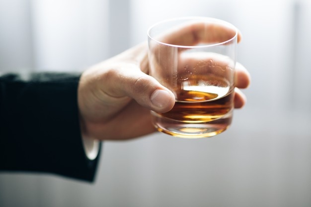 man holding glass of whiskey in black suit 