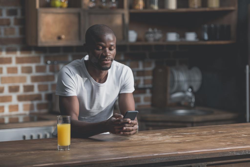 African american man using phone while sitting in kitchen 