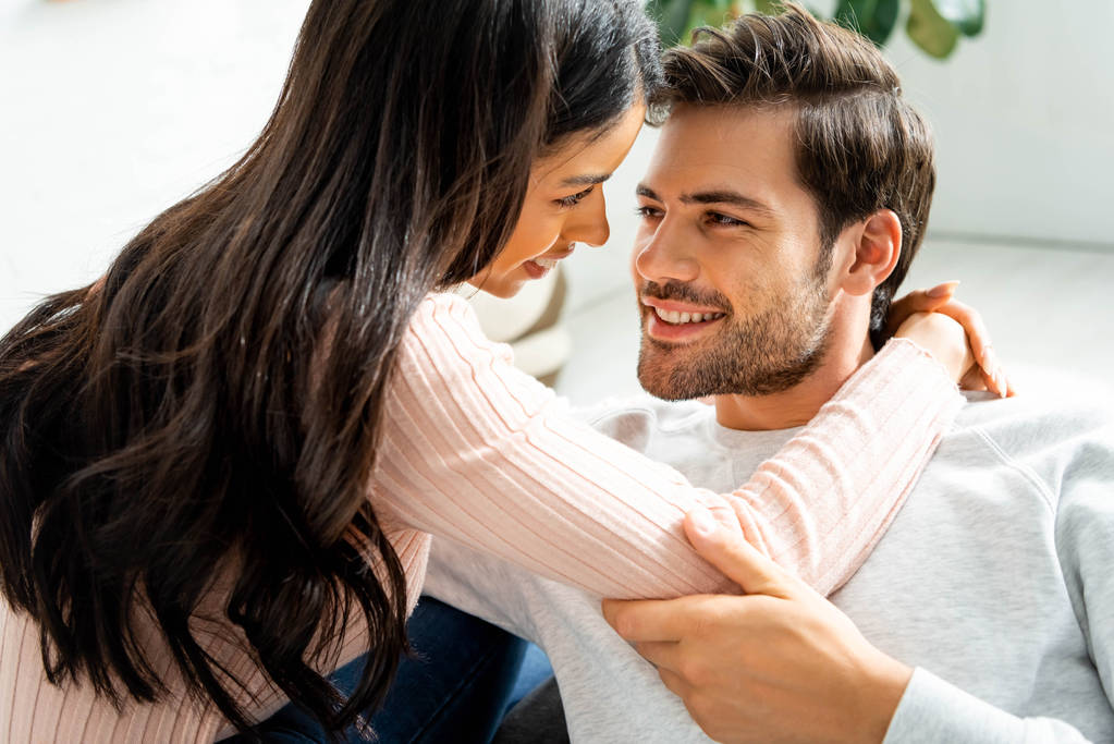 american woman and handsome man smiling and hugging in apartment