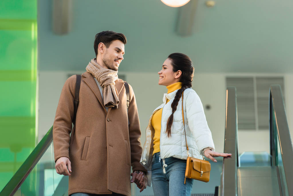 couple holding hands, looking at each other and going down on escalator
