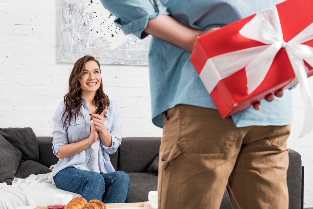 man holding red birthday present behind back with excited woman