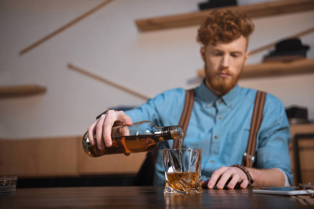 young man pouring whisky from bottle in glass