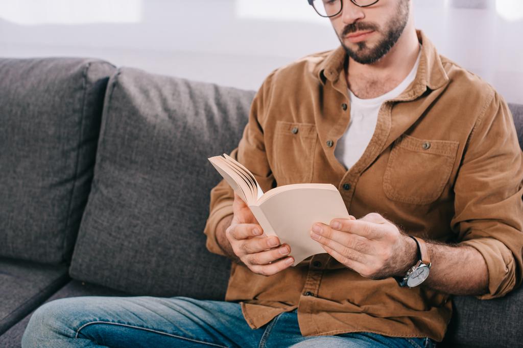 bearded man in eyeglasses reading book at home