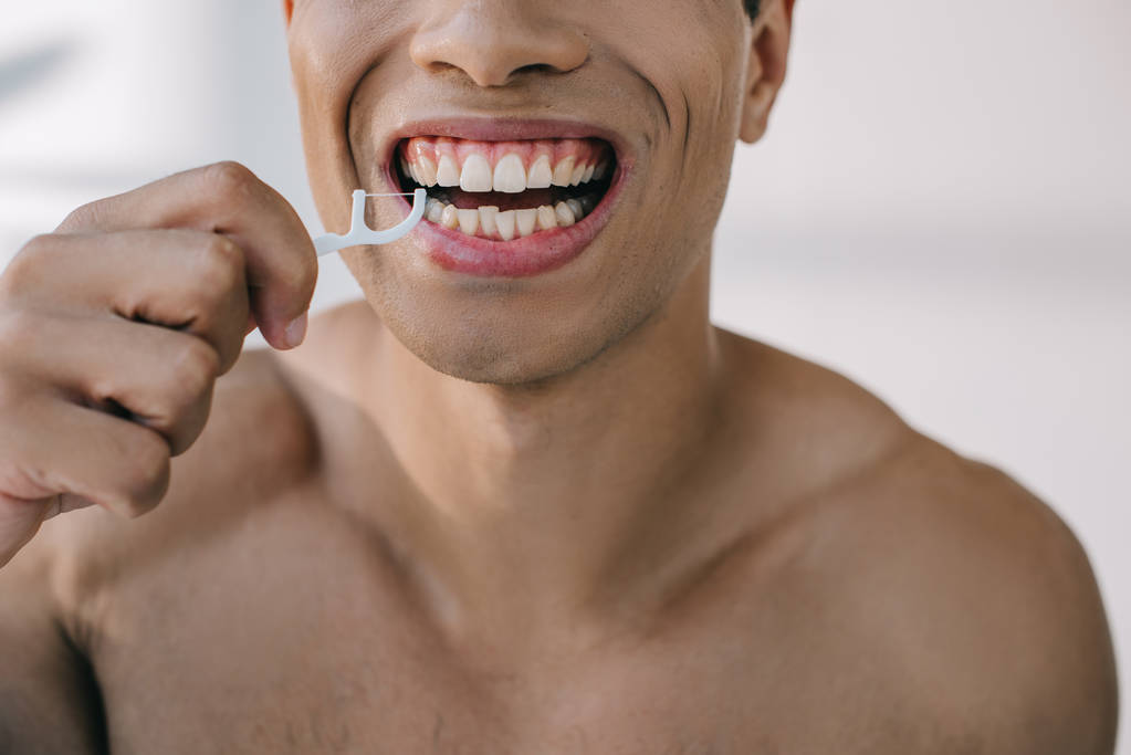 mixed race man using dental floss on stick