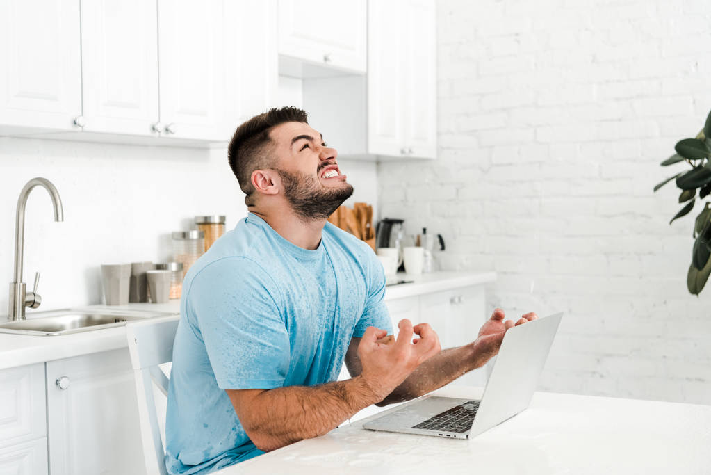 man gesturing while looking up near laptop in kitchen