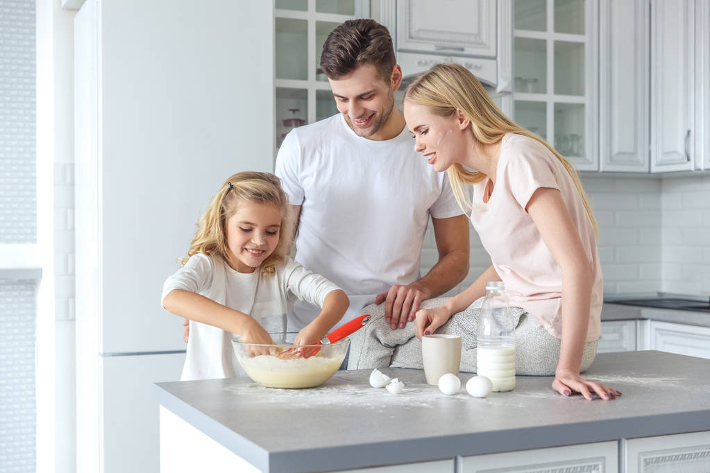 Parents teaching their daughter to cook at kitchen