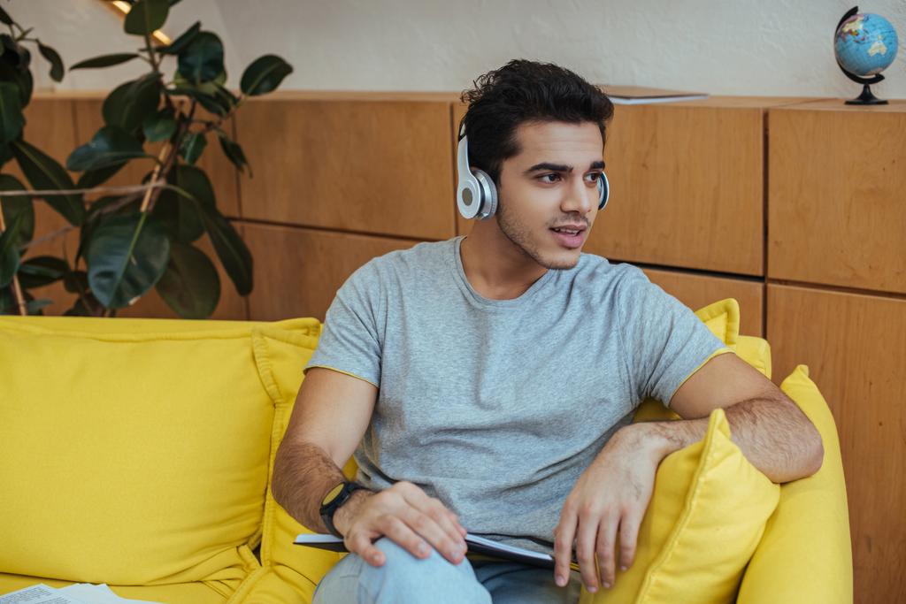 Freelancer in headphones with notebook looking away on sofa