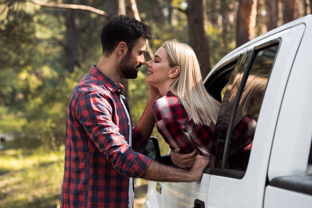 Happy boyfriend going to kiss smiling girlfriend while she sitting in pickup truck 