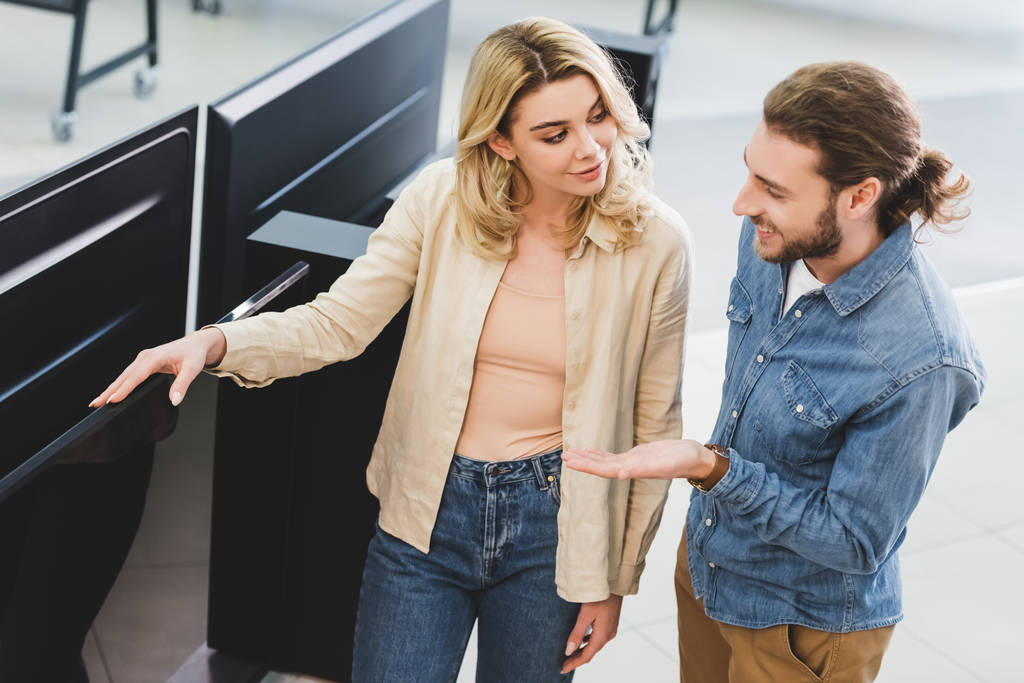 smiling boyfriend pointing with hand at new tv and talking with girlfriend in home appliance store