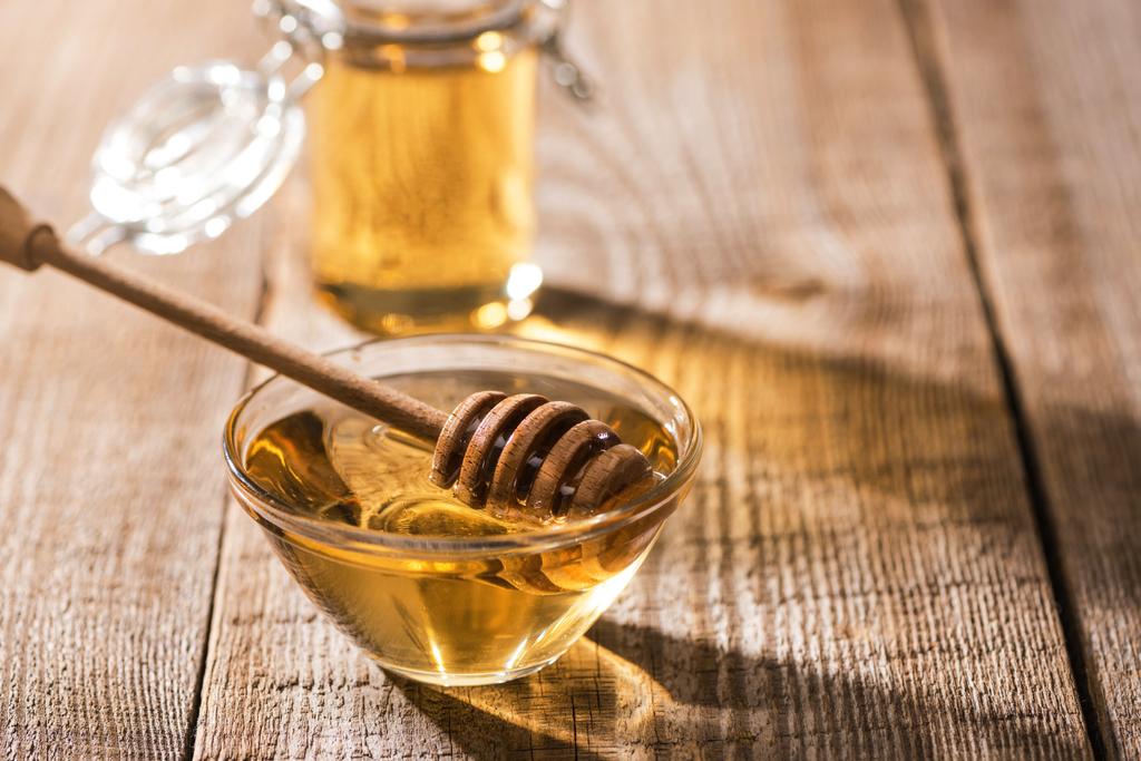 Jars with honey and honey dipper on wooden table in sunlight