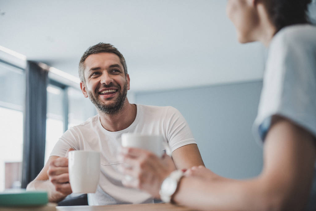 smiling couple drinking coffee and talking at table at home
