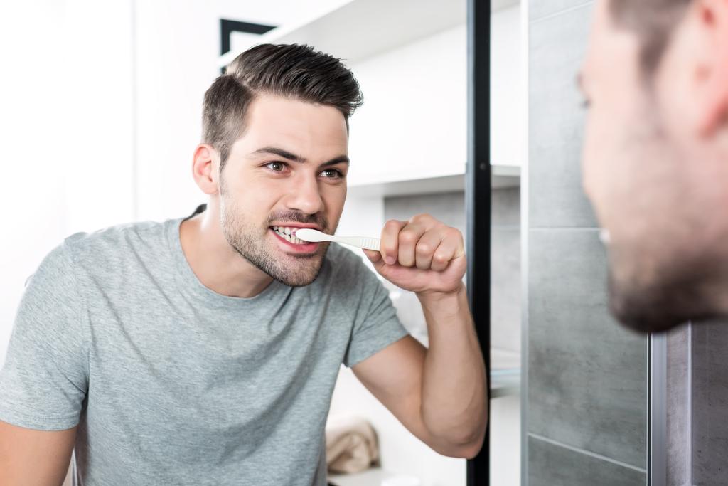 Young man brushing teeth and looking at mirror