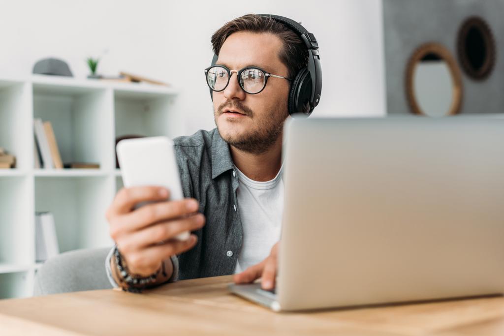 Young handsome man in headphones using smartphone and looking away