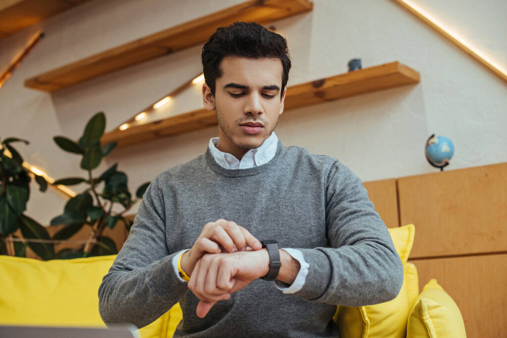 Man looking at wristwatch on sofa in living room