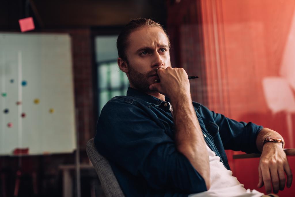 Pensive businessman holding pen while thinking in office