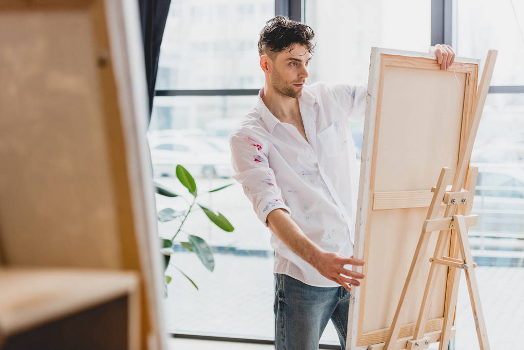  handsome artist fixing canvas on easel in gallery