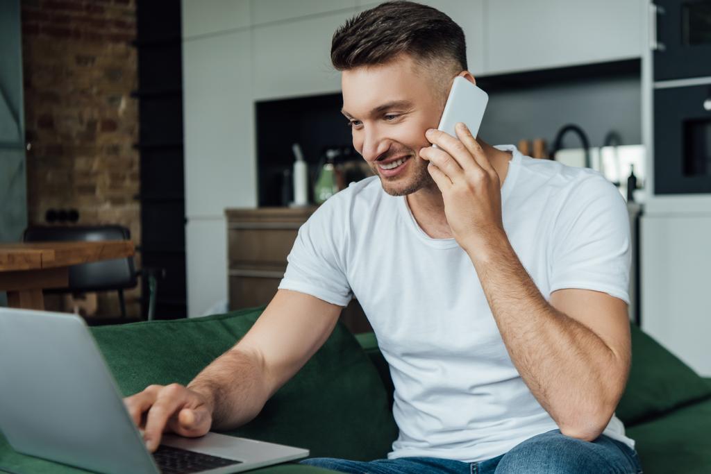 smiling teleworker talking on smartphone and using laptop at home 