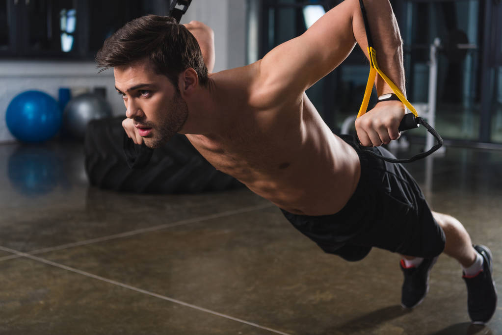 Shirtless sportsman training with elastics in sports hall