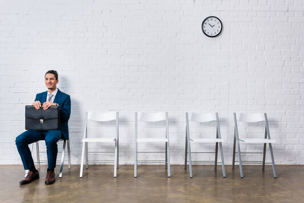 Smiling man with briefcase waiting for interview while sitting on chair