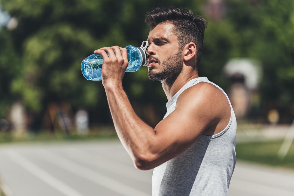 Sporty young man drinking water after workout