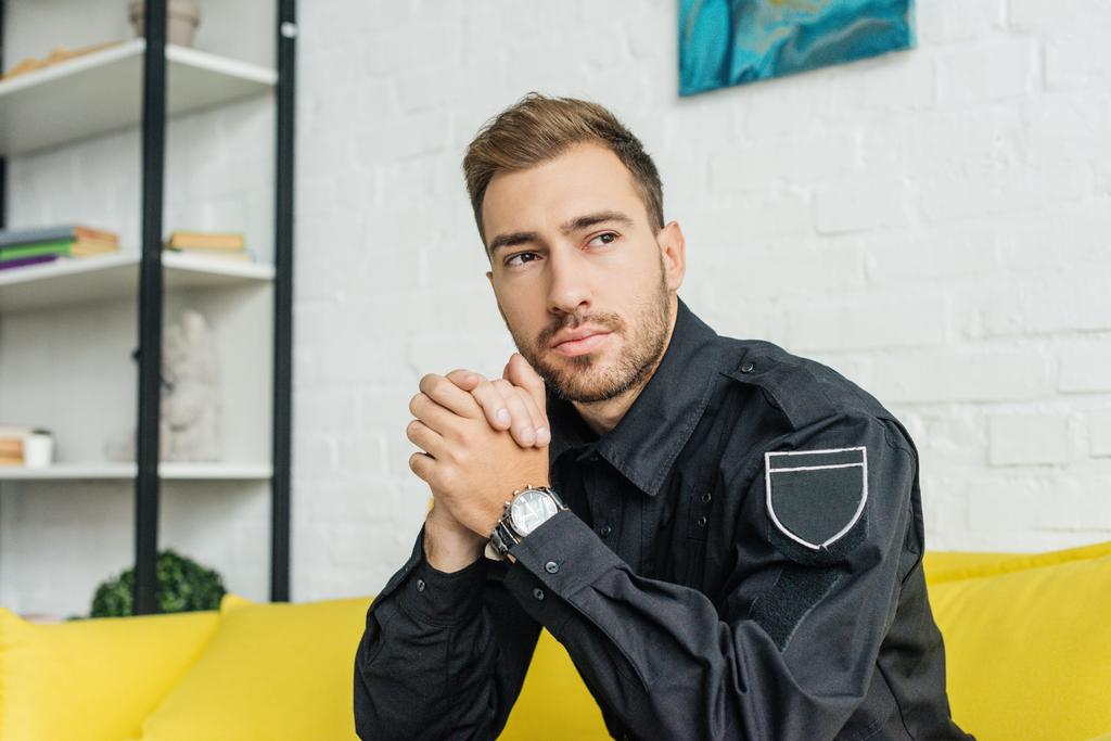 Thoughtful young policeman sitting on yellow couch