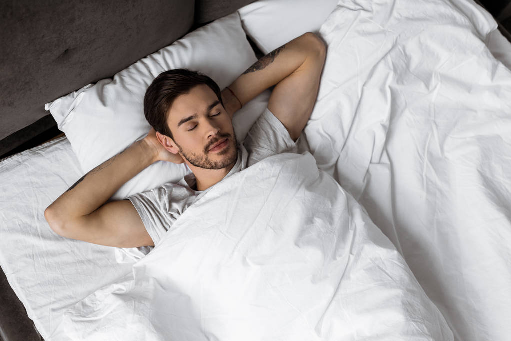  handsome bearded young man sleeping with hands behind head in bed