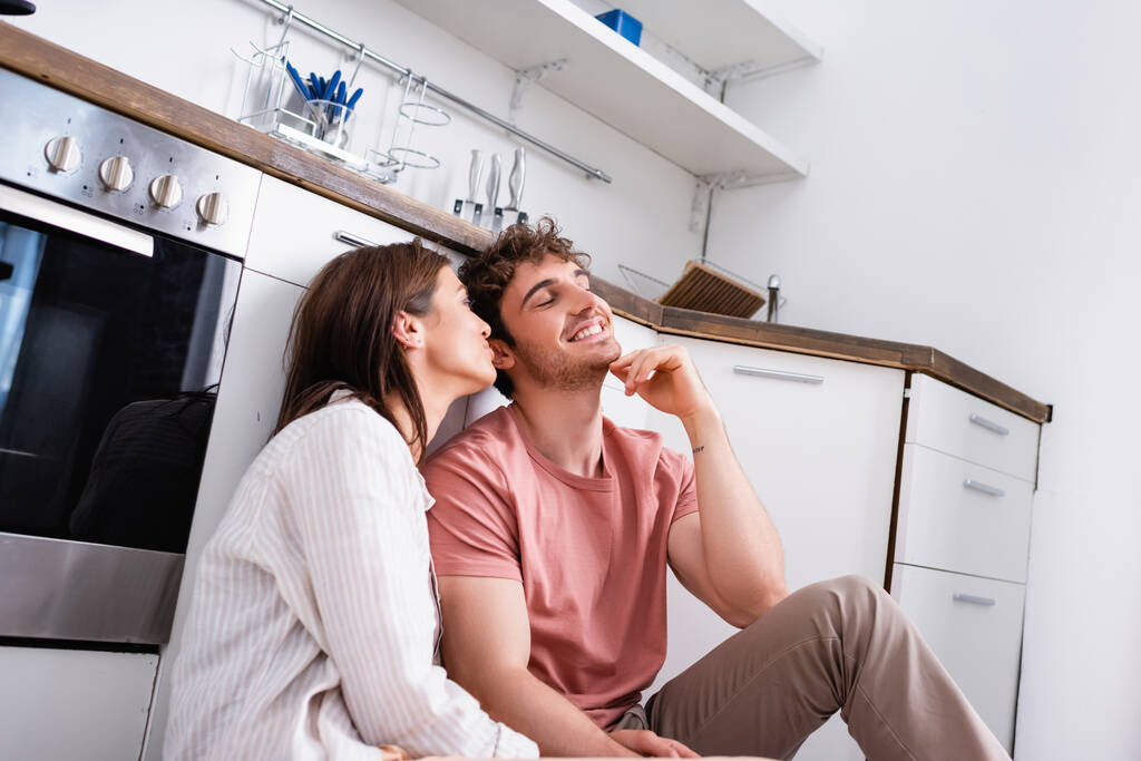 Young woman sitting near smiling man in kitchen