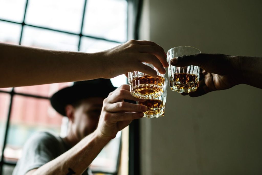 men clink glasses of whiskey drink alcoholic beverage together