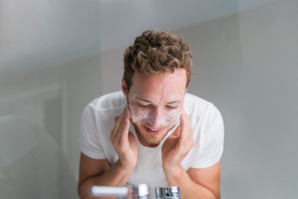 Man washing face with facial cleanser face wash soap in bathroom sink at home