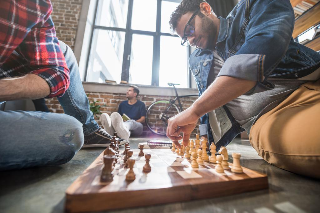 men sitting on floor and playing chess on chess board