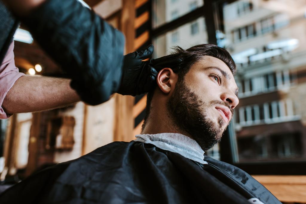 barber in latex gloves holding hair comb while styling hair of man